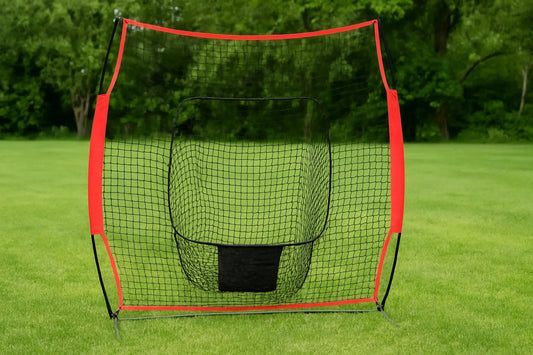 A portable sports backstop net with a red frame and black mesh stands on a green field, with trees in the background under soft daylight.