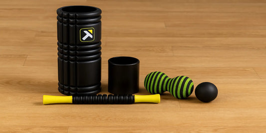 A complete 5-in-1 foam roller set including a grid roller, massage stick, peanut ball, and more, neatly arranged on a wooden floor.